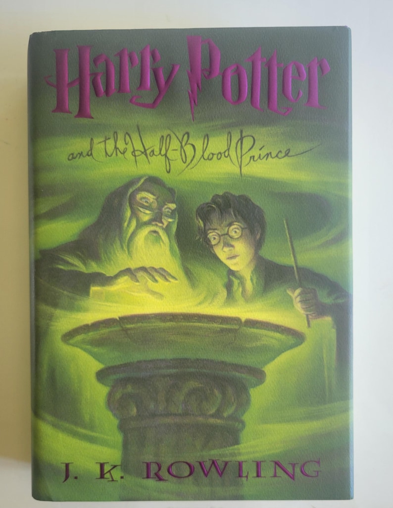 May include: The cover of "Harry Potter and the Half-Blood Prince" by J.K. Rowling. The book has a purple title, with illustrations of Dumbledore, Harry Potter, and a green cauldron.