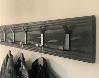May include: A black wooden coat rack with five metal hooks. Three jackets are hanging on the hooks.