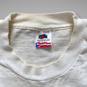 May include: White Fruit of the Loom t-shirt tag with a red, white and blue logo and the text "Fruit of the Loom" and "100% Cotton Preshrunk Made in U.S.A."