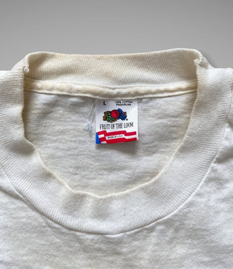 May include: White Fruit of the Loom t-shirt tag with a red, white and blue logo and the text "Fruit of the Loom" and "100% Cotton Preshrunk Made in U.S.A."