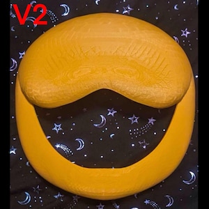May include: A yellow, wooden, circular object with a curved top and a crescent-shaped opening. The object is set against a black background with white stars and crescent moons. The text "V2" is in the upper left corner.