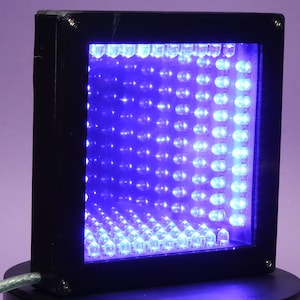 Peut inclure: Une boîte carrée noire avec un cadre noir, contenant une grille de lumières LED bleues. Les lumières créent une illusion d'optique qui semble être un tunnel.