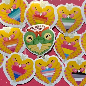 May include: A collection of die-cut stickers featuring yellow worm-like creatures forming heart shapes around various pride flag patterns. One central sticker depicts two green caterpillars forming a heart with the text YOU KEEP ME WORM.