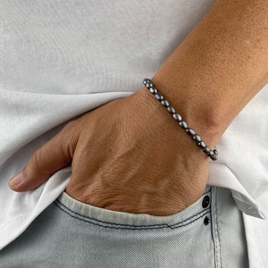 Könnte beinhalten: Ein graues Armband mit ovalen Perlen.