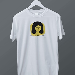 Könnte beinhalten: Weißes T-Shirt mit einer gelben und schwarzen Illustration einer Frau mit dem Text "that's hilarious."