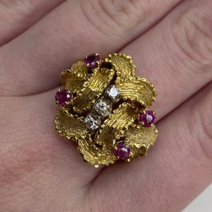 Puede incluir: Un anillo de oro con un diseño texturizado que presenta cinco rubíes rojos y un grupo de diamantes.