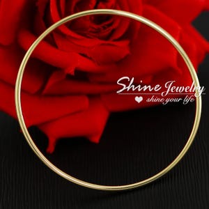 May include: A gold bangle bracelet, set against a red rose and a black background. The thin, circular bracelet is the focal point. White script reads "Shine Jewelry shine your life".