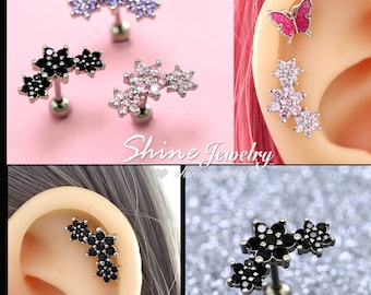 May include: Three pairs of earrings with a flower design. The earrings are made of silver and have black, pink, and purple crystals. The earrings are shown on a model's ear.