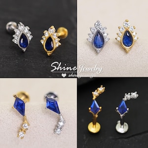 May include: A collection of stud earrings featuring pear-shaped and kite-shaped blue stones accented with clear crystals. The jewellery is available in silver and gold tones, with some designs showcasing a tiered arrangement of stones. Text reads Shine Jewelry.