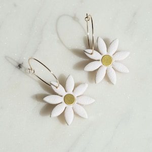 Könnte beinhalten: Ein Paar goldene Creolen mit weißen Gänseblümchen-Anhängern. Die Mitte jeder Blume hat einen goldenen Kreis.