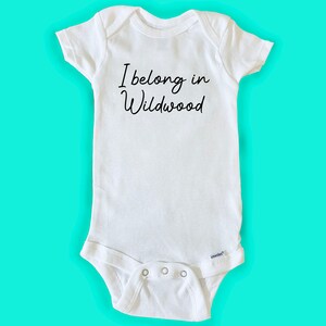 May include: White baby onesie with black text that reads "I belong in Wildwood".