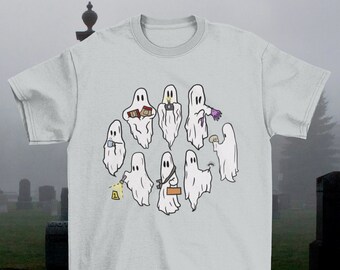 May include: A light gray t-shirt with a graphic of a group of ghosts holding various objects, including a book, a camera, a cup, a flashlight, a hammer, and a skull. The ghosts are all white and have a cartoonish appearance.