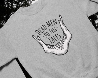 May include: A light gray sweatshirt featuring a black and white illustration of a jawbone with the text "DEAD MEN DO TELL TALES" in a gothic font. The sweatshirt is made of a soft material.