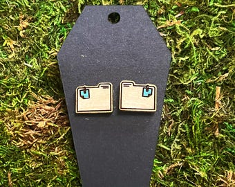 May include: A pair of wooden earrings shaped like folders with blue accents. The earrings are displayed on a black coffin-shaped stand.