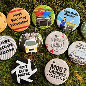 May include: Ten round buttons with different designs and text. The buttons are white, black, green, and beige with black text. The text on the buttons includes "Most Firearm Hits", "Most Evidence Processed", "Most Major Cases", "Most Media Moments", "Most Latent Idents", "Most Calls for Service", "Most Death Calls", "Trainer of the Year", "Most DNA Hits", "Most Scene Photos", and "Most Casings Collected".