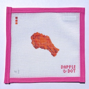 May include: A square needlepoint canvas featuring a central orange and red chicken wing design. The canvas has a bright pink fabric border and white grid mesh. The text DAPPLE & DOT is printed in red in the bottom right corner, with small red squares in the top left.