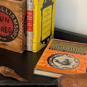 May include: A collection of antique books, including "Primer of American Antiques" and "The Collecting of Antiques." The books are in various colors, with a wooden box and a yellow book titled "Care and Repair of Antiques."
