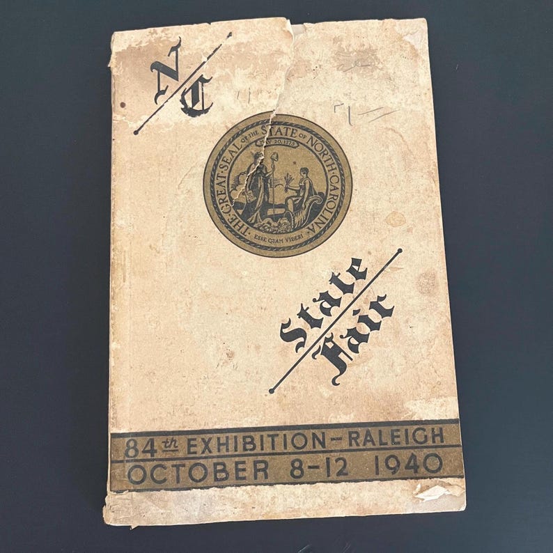 May include: Vintage State Fair program from Raleigh, North Carolina, featuring the state seal and the text "State Fair." The cover is aged with visible wear and tear, and the date "October 8-12 1940" is printed at the bottom.