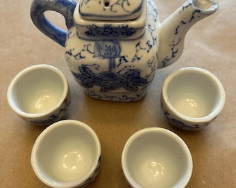 May include: A blue and white porcelain tea set with a teapot and four cups. The teapot has a floral design and a lid. The cups are plain white.