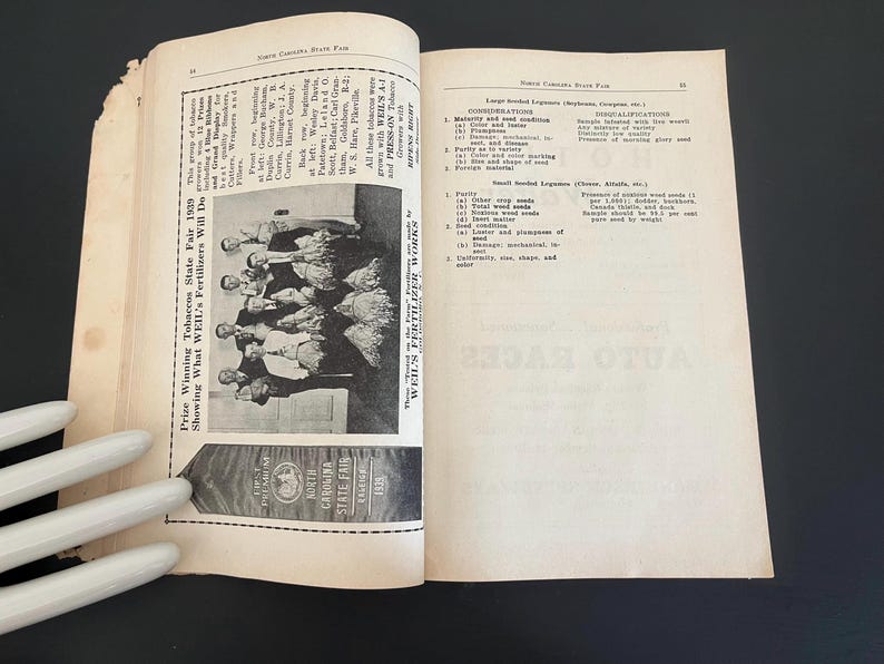 May include: Open book with pages featuring text and a black and white photograph of a group of people. The left page has text about the North Carolina State Fair 1939. A ribbon reads "First Premium North Carolina State Fair 1939."