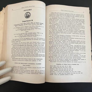 May include: Open book pages with text about poultry, Department H, and the North Carolina State Fair. The pages are aged with a worn appearance. The text includes rules, regulations, and definitions.