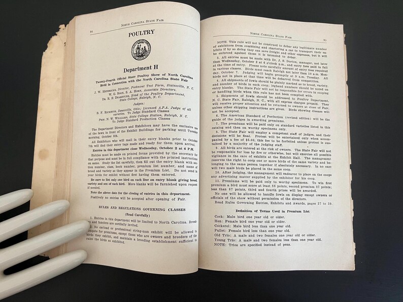 May include: Open book pages with text about poultry, Department H, and the North Carolina State Fair. The pages are aged with a worn appearance. The text includes rules, regulations, and definitions.