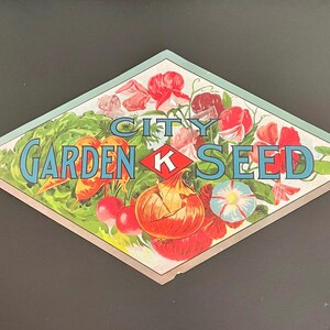 May include: Vintage diamond-shaped seed packet featuring the text "City Garden Seed K". The illustration includes colorful vegetables and flowers, such as radishes, onions, and sweet peas, with a light blue and green border.