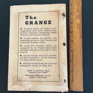 May include: A vintage pamphlet for The Grange, an agricultural organization, with text in black on aged paper. The pamphlet includes bullet points detailing the organization's benefits and contact information for North Carolina representatives. A wooden ruler is next to the pamphlet.