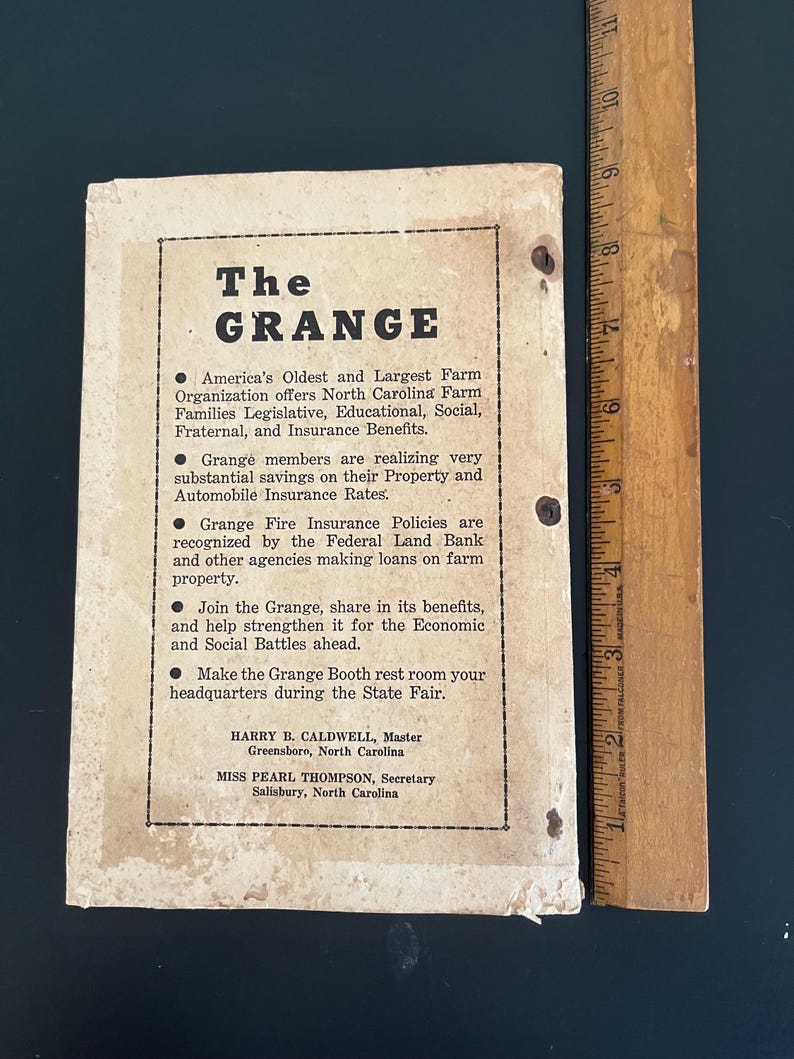 May include: A vintage pamphlet for The Grange, an agricultural organization, with text in black on aged paper. The pamphlet includes bullet points detailing the organization's benefits and contact information for North Carolina representatives. A wooden ruler is next to the pamphlet.