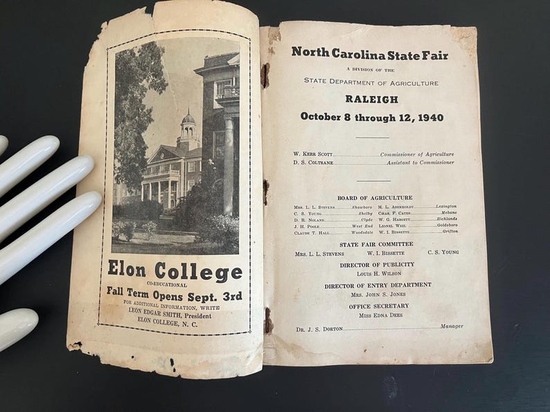 May include: Open vintage pamphlet for the North Carolina State Fair in Raleigh, October 8-12, 1940. The left page features a black and white image of Elon College with text: "Fall Term Opens Sept. 3rd."