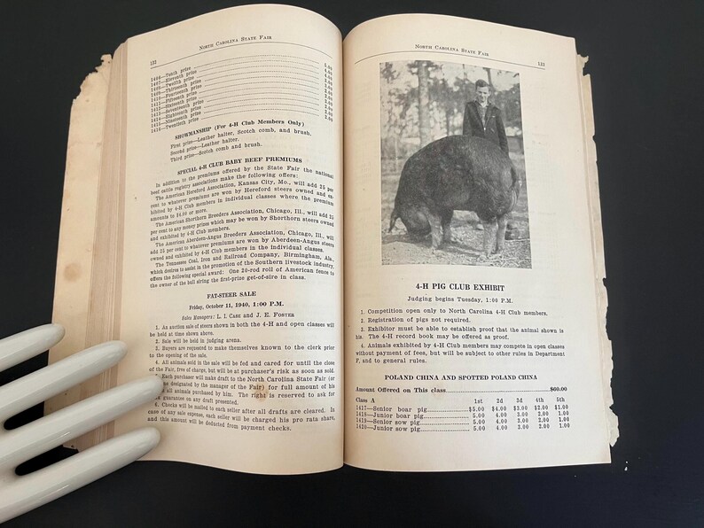 May include: An open book with aged pages, featuring text and a black and white photograph of a pig at a 4-H Pig Club Exhibit. The text includes details about the exhibit and a sale.