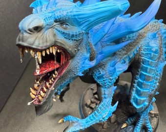 May include: A detailed figurine of a dragon with a wide open mouth, showcasing sharp teeth and a red interior. The dragon features blue horns and accents, with a gray and blue body. The figurine is set on a dark, textured base.
