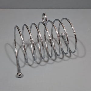 May include: A chrome-finished, spiral-shaped letter holder. The holder features a series of circular loops connected by a central support, with a small loop at the top and a rounded base. The design is sleek and modern.