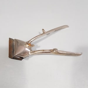 May include: A vintage silver-toned hair clipper with a long handle and a comb attachment. The clipper has a worn, aged look.