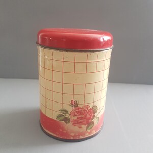 Può includere: Contenitore vintage in metallo con coperchio rosso e corpo color crema. Il corpo presenta un motivo a griglia rosso e crema e un grande design a rosa rosa. Un affascinante contenitore da cucina.