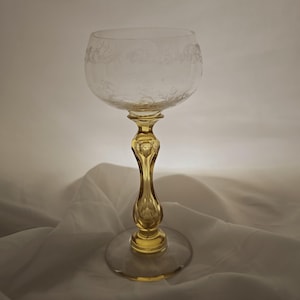 May include: A clear glass goblet featuring a delicate etched floral pattern around the bowl. The stem is crafted from translucent yellow glass with a faceted, bulbous design, connecting to a clear, circular glass base for stability.