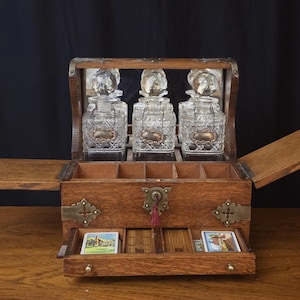 May include: An antique wooden vanity chest with three glass perfume bottles. The chest has a hinged lid, a pull-out drawer with small cards, and brass hardware. The bottles have ornate stoppers and silver-colored labels.