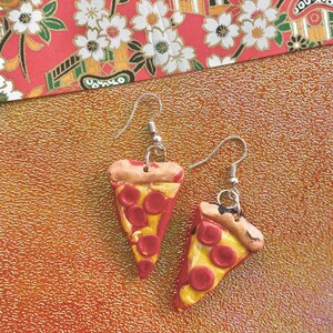 May include: A pair of silver dangle earrings featuring handmade polymer clay pizza slices with red pepperoni and yellow cheese.
