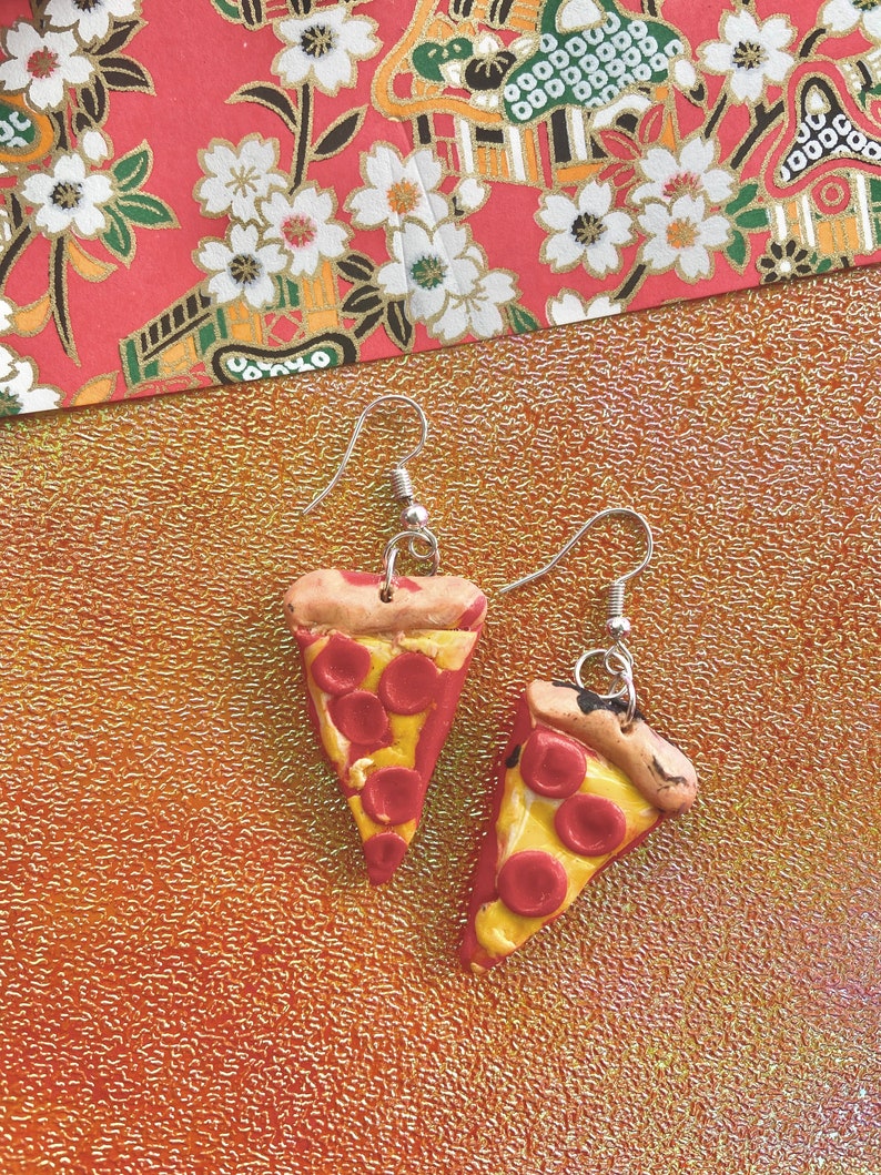 Op de afbeelding: Een paar zilveren oorhangers met handgemaakte pizzapunten van polymer clay met rode pepperoni en gele kaas.