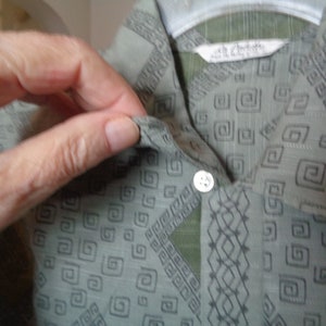 May include: A green button-up shirt with a geometric pattern. The shirt has a single button closure at the neck.