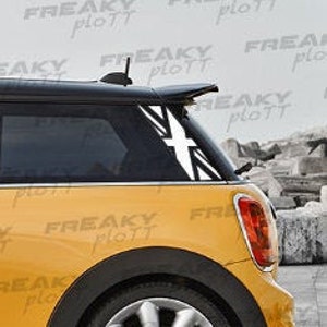 Può includere: Una Mini Cooper gialla con un adesivo Union Jack bianco e nero sul lunotto posteriore. L'adesivo è una versione stilizzata della bandiera britannica.