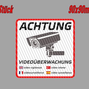 Könnte beinhalten: Zwei quadratische Warnschilder in Rot und Weiß mit der Aufschrift "ACHTUNG VIDEOÜBERWACHUNG" in Schwarz. Die Schilder zeigen außerdem eine schwarz-weiße Silhouette einer Überwachungskamera und den Text "video vigilancia", "vidéosurveillance", "video izleme" und "video surveillance" in Englisch, Französisch, Türkisch und Spanisch.
