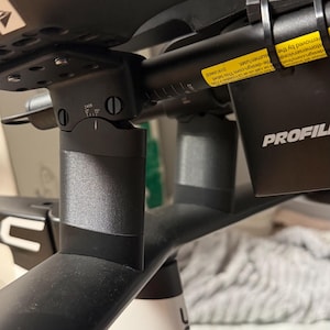 Könnte beinhalten: Ein schwarzes Fahrrad-Cockpit mit matten Profile Design Aero-Lenkern. Die Baugruppe umfasst einen zentralen Vorbau, verstellbare Armauflagen und ein gelbes Warnetikett am Lenker. Der Rahmen ist weiß und schwarz gehalten und trägt den Schriftzug BMC.