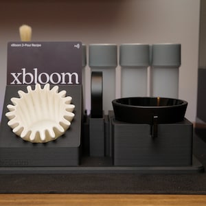 以下が含まれることがあります： 白いフィルター、黒いボウル、3つのグレーの容器が付いた黒いコーヒー醸造ステーション。ステーションには「xbloom」という文字が印刷されています。