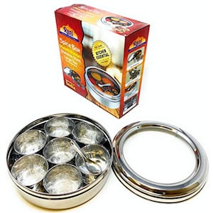May include: A stainless steel spice box with seven compartments and a small spoon, next to its packaging. The box is round and has a clear lid. The packaging is red and brown with the text "Spice Box" and "Kitchen Essential".
