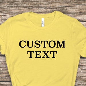 May include: A light yellow t-shirt with the text "CUSTOM TEXT" printed in black on the front.