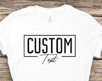 May include: White t-shirt with a black box around the text "CUSTOM Text" on a wooden background.