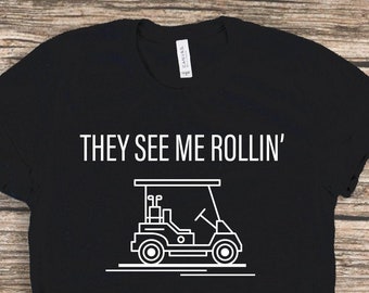 May include: Black t-shirt with white text that reads "They See Me Rollin'" and a graphic of a golf cart.