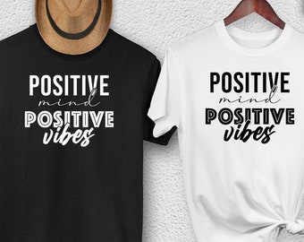 May include: Two t-shirts with the text "POSITIVE mind POSITIVE vibes" printed on them. One t-shirt is black and the other is white.