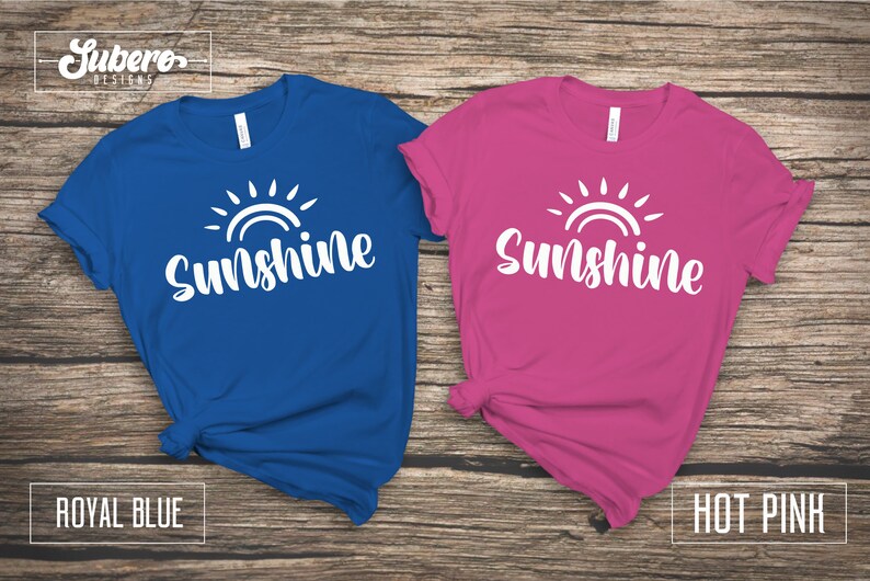 May include: Two t-shirts with a white sun and the word "Sunshine" printed on them. The shirt on the left is royal blue and the shirt on the right is hot pink.